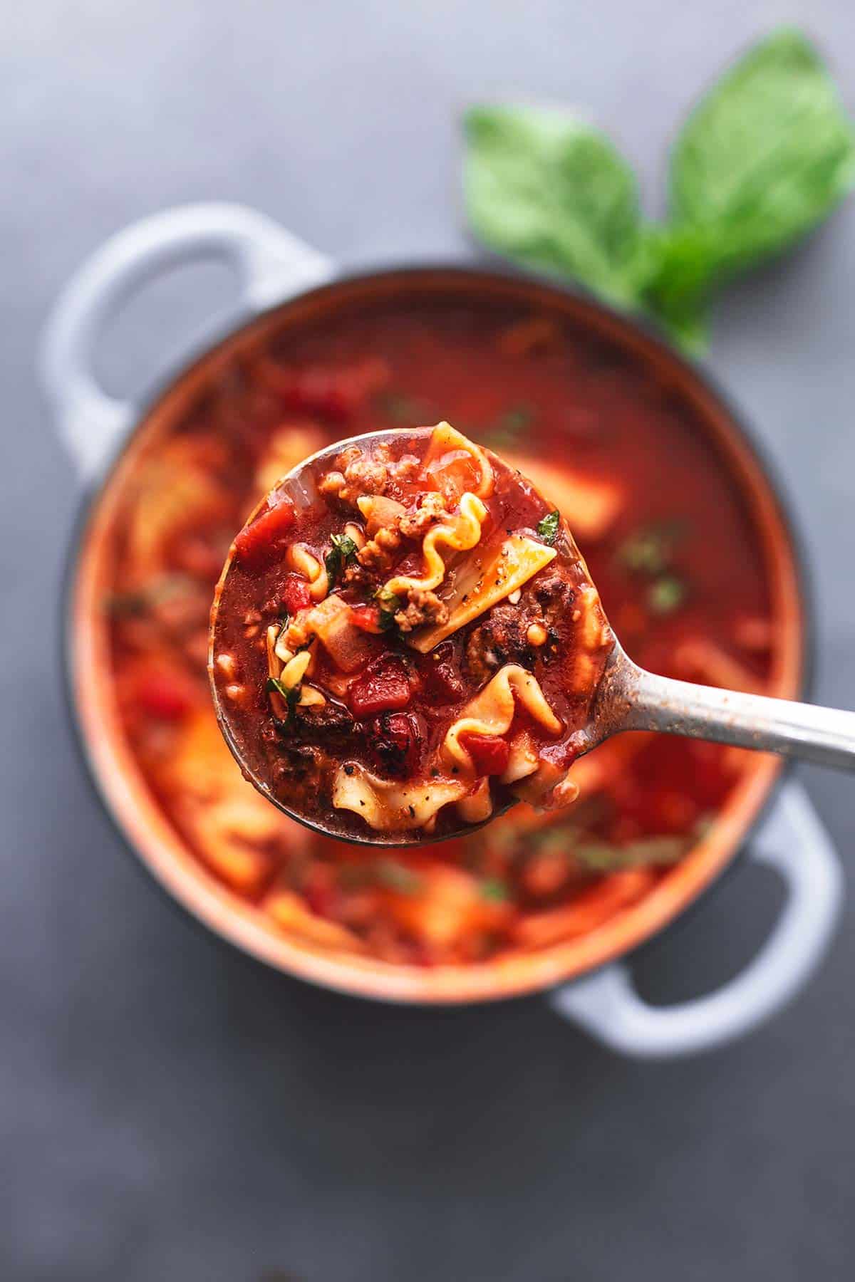 overhead view of ladle full of red soup with ground sausage and noodles