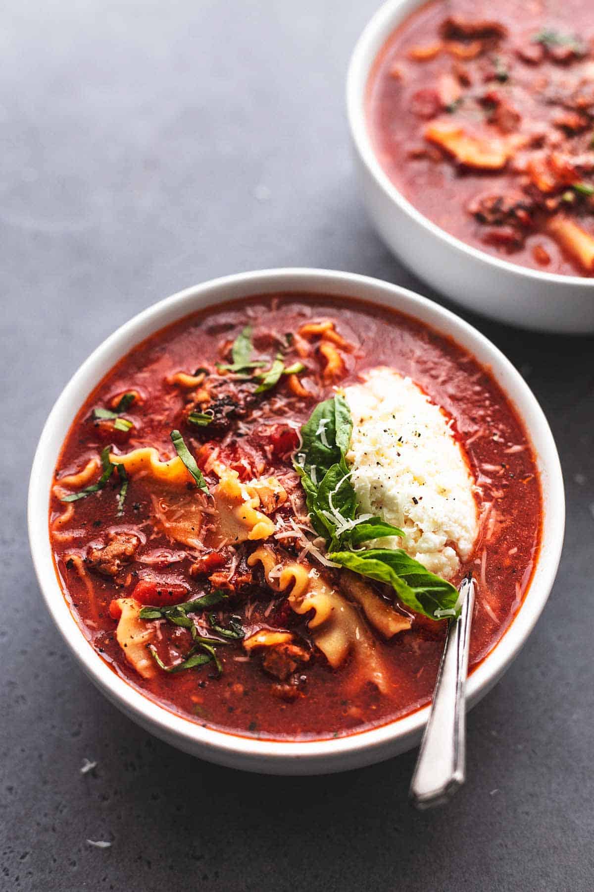 lasagna soup in bowl with spoon, ricotta, and fresh basil garnish
