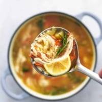 overhead view of ladle full of soup with orzo and chicken and carrots and a lemon wedge