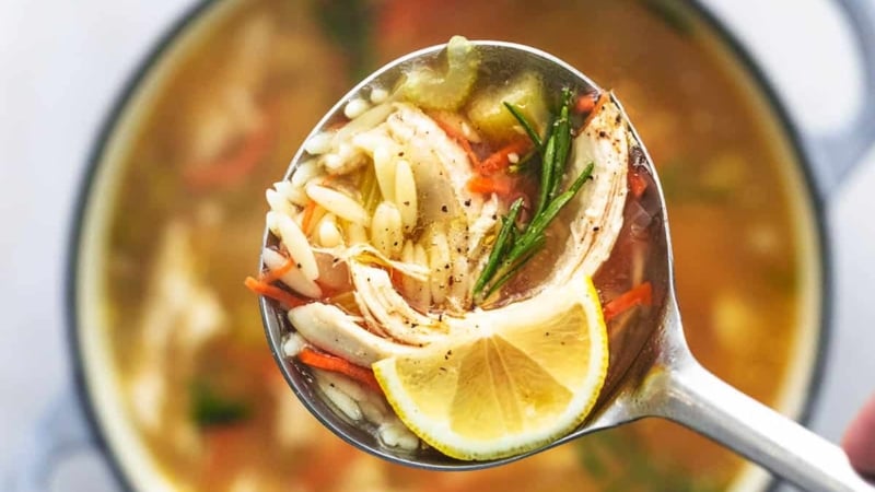 overhead view of ladle full of soup with orzo and chicken and carrots and a lemon wedge