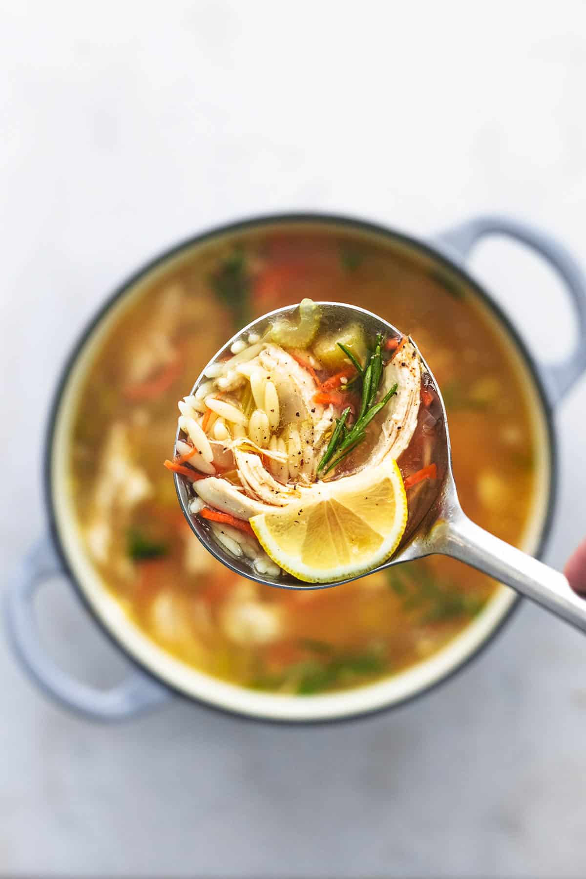 overhead view of ladle full of soup with orzo and chicken and carrots and a lemon wedge