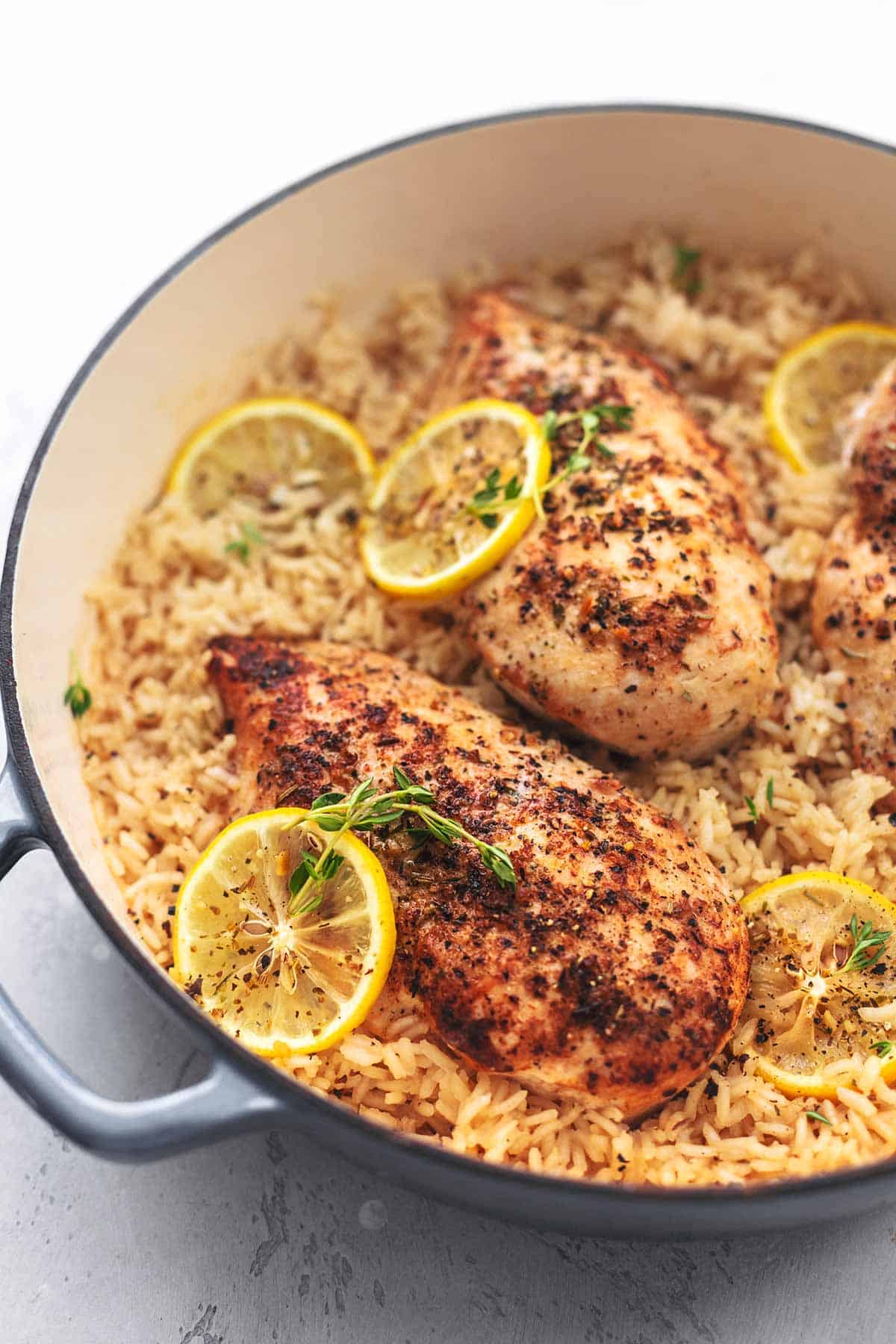 close up of lemon herb chicken and rice with lemon wheels in a skillet.