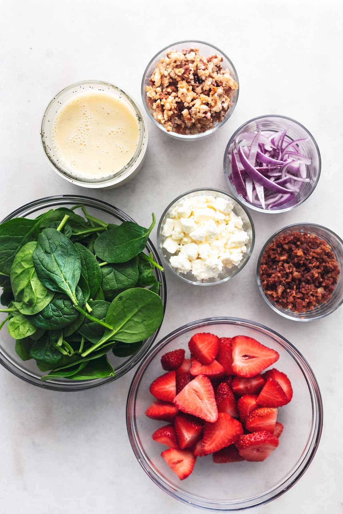 overhead view of ingredients for spinach salad with strawberries and bacon on marble tabletop