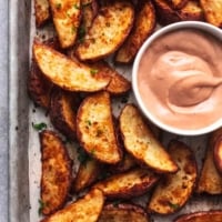 browned crispy potato wedges on baking sheet with pink-brown dipping sauce in white bowl