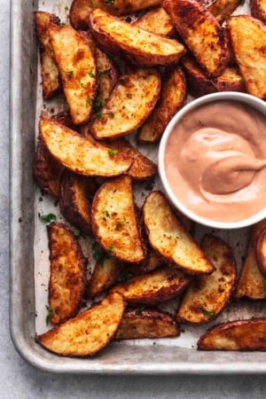 browned crispy potato wedges on baking sheet with pink-brown dipping sauce in white bowl