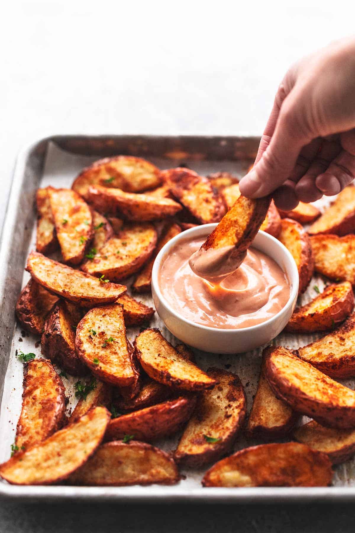 hand dipping single baked potato wedge into brown sauce in front of more potato wedges