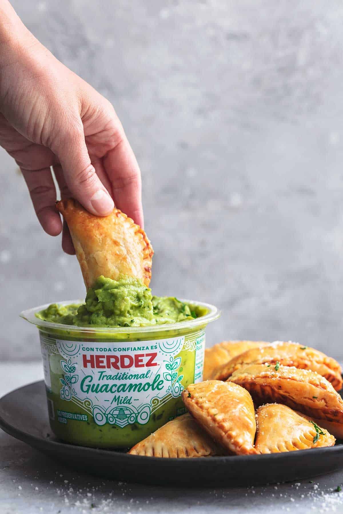 hand dipping empanada into container of Herdez guacamole