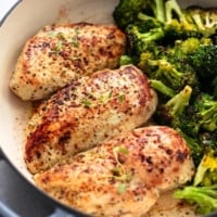 three seasoned, cooked chicken breasts in skillet beside broccoli