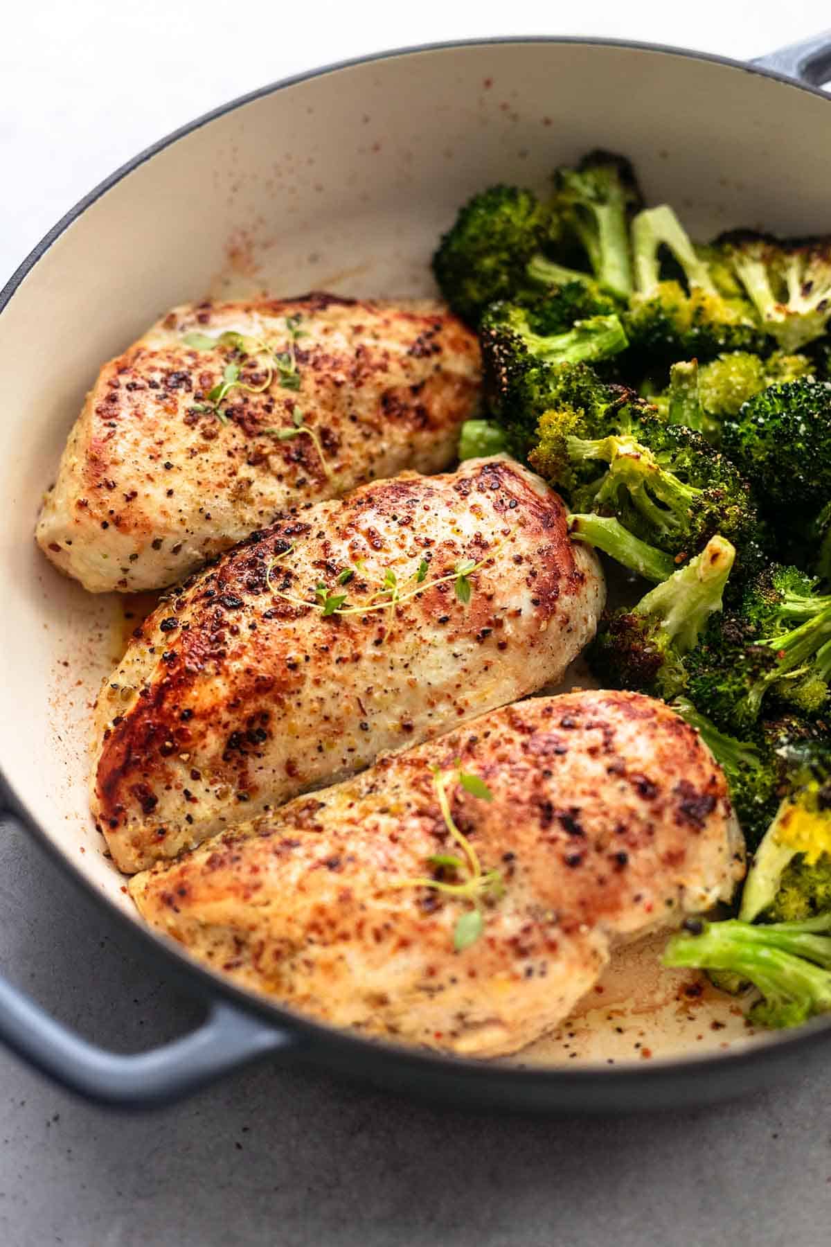three seasoned, cooked chicken breasts in skillet beside broccoli