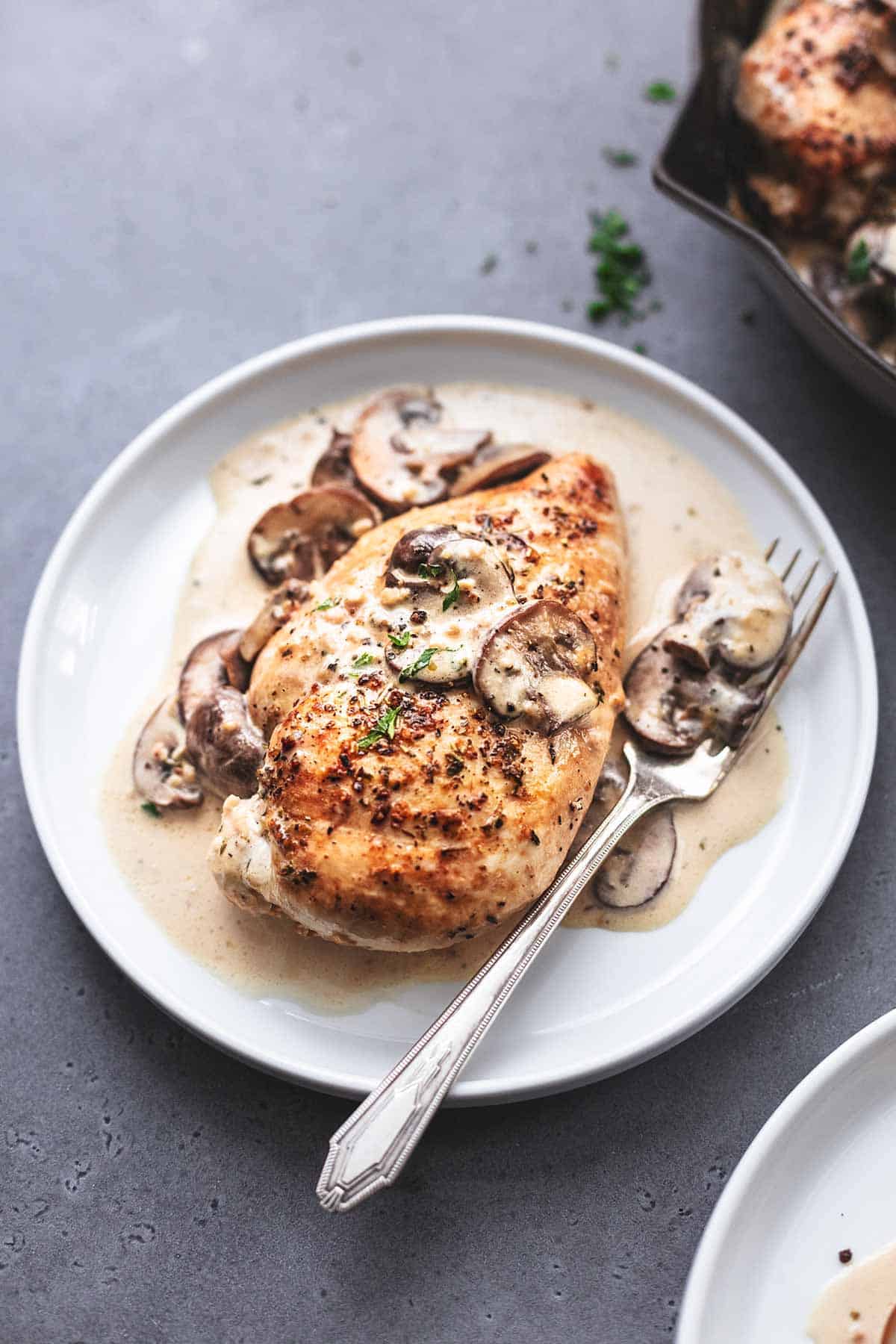 single cooked chicken breast with mushroom sauce with fork on white plate
