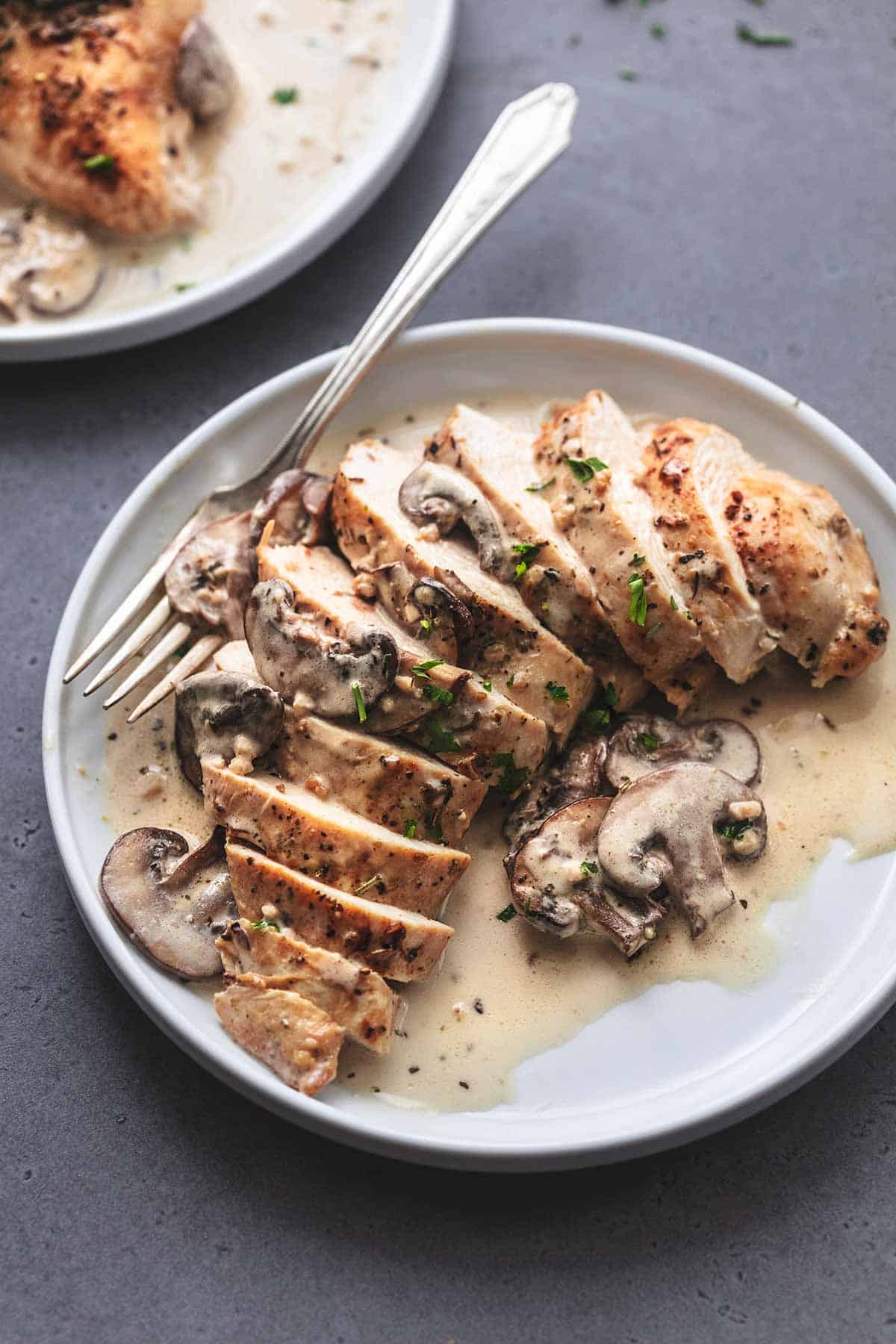 sliced cooked chicken breast on a white plate with brown sauce and sliced mushrooms