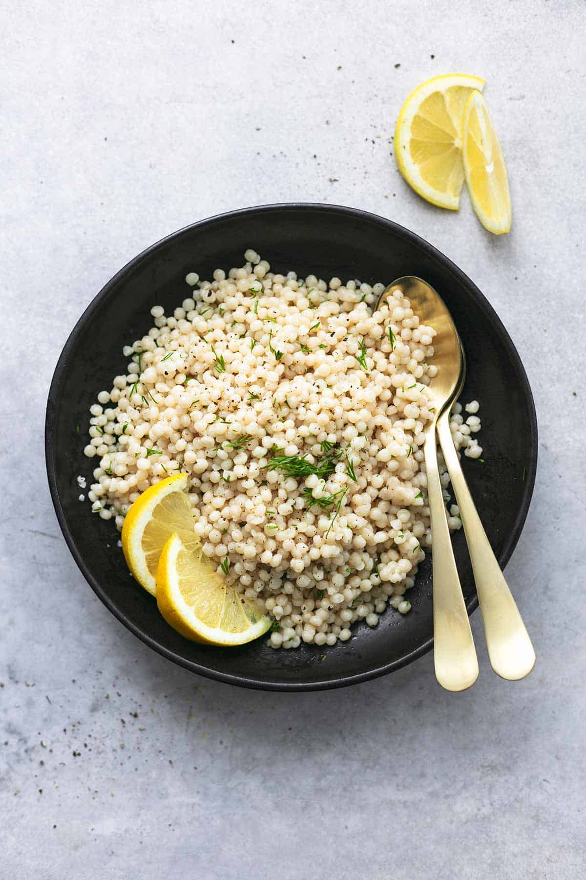top view of lemon couscous with lemon wedges and two spoons in a bowl.