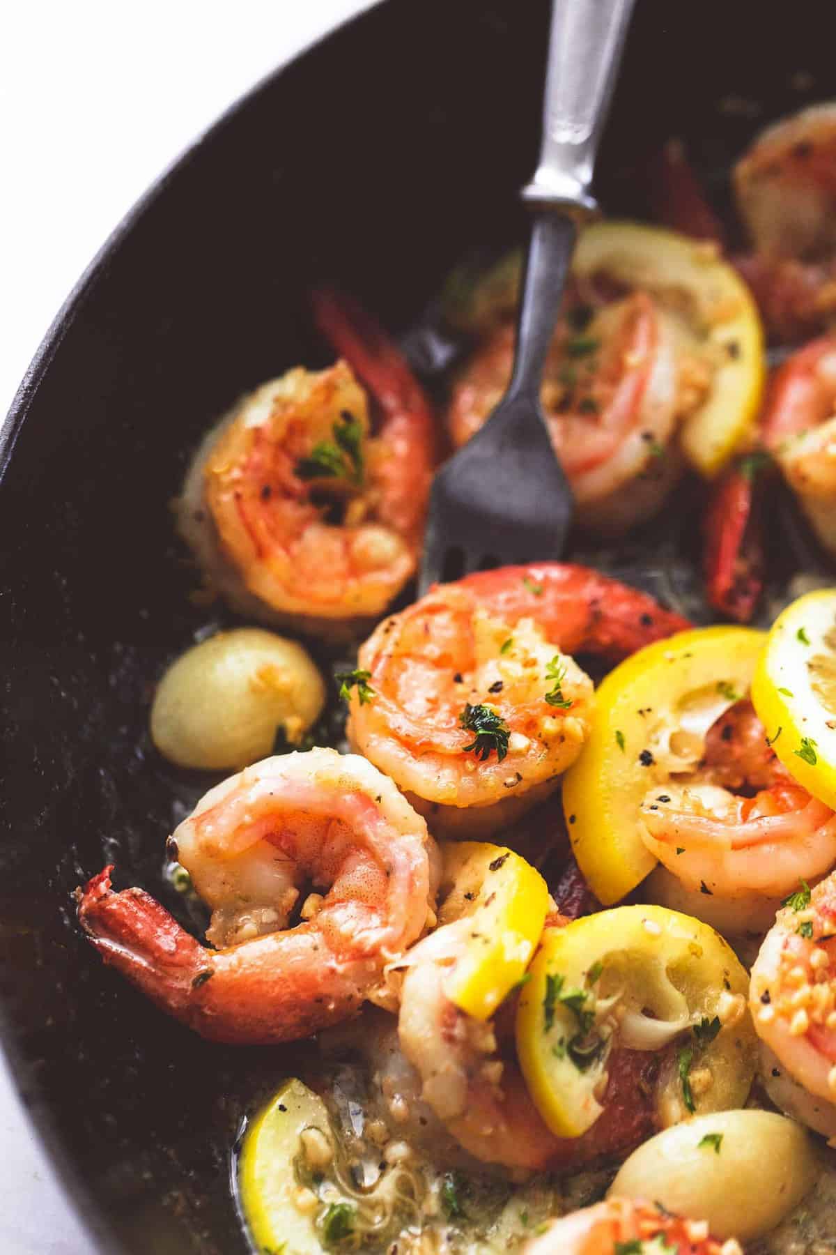 close up of lemon garlic butter shrimp with a fork in a pan.