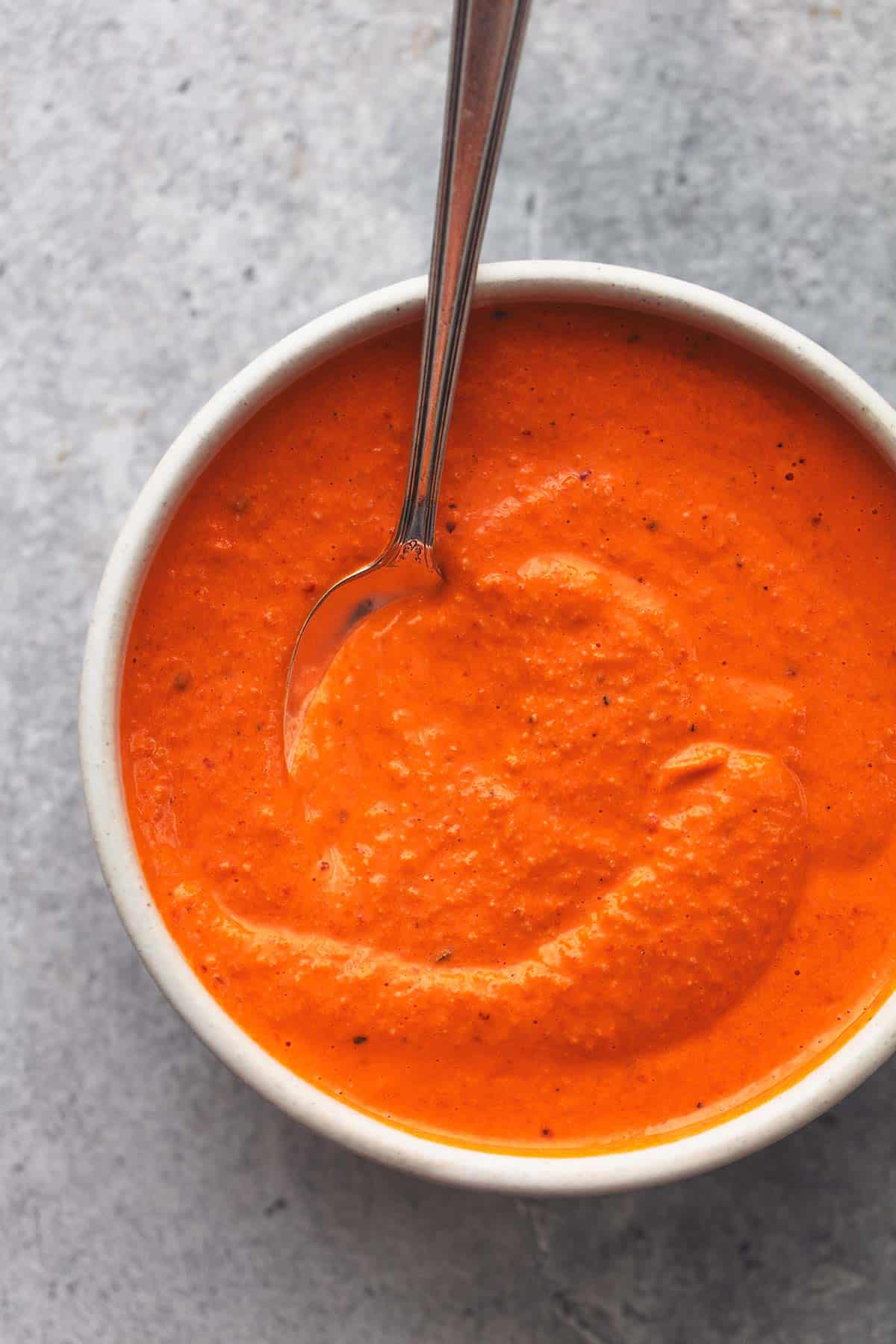 close up top view of roasted red pepper sauce with a spoon in a bowl.