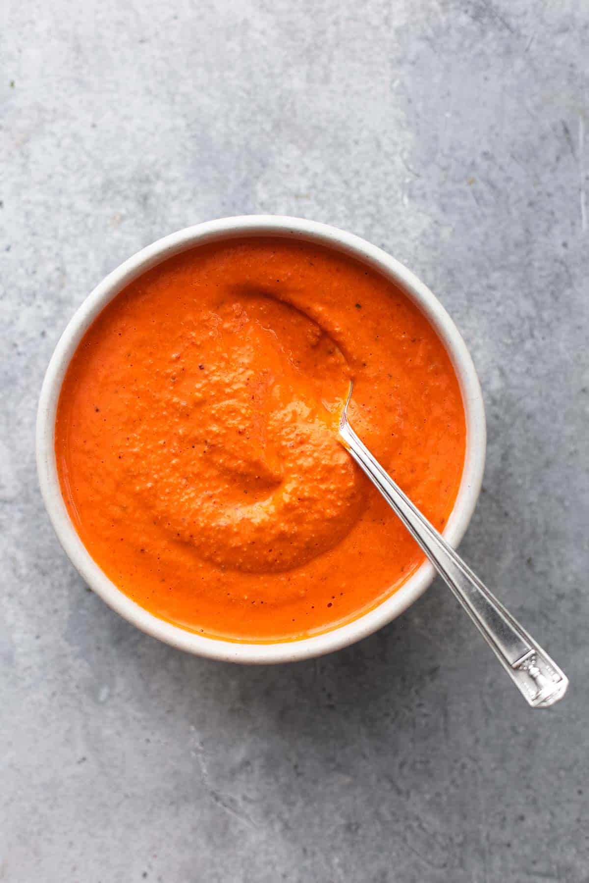 top view of roasted red pepper sauce with a spoon in a bowl.