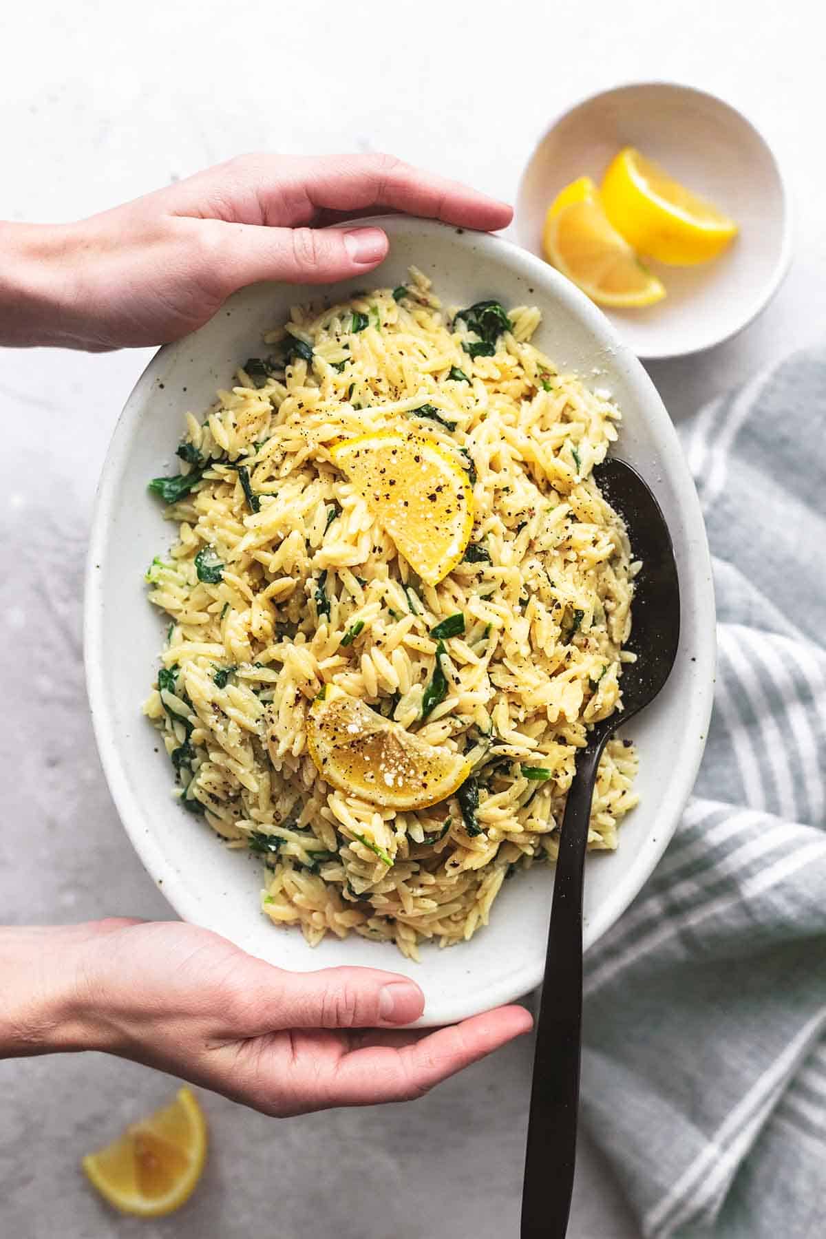 top view of hands holding creamy parmesan spinach orzo on a plate above green striped linen on gray table.