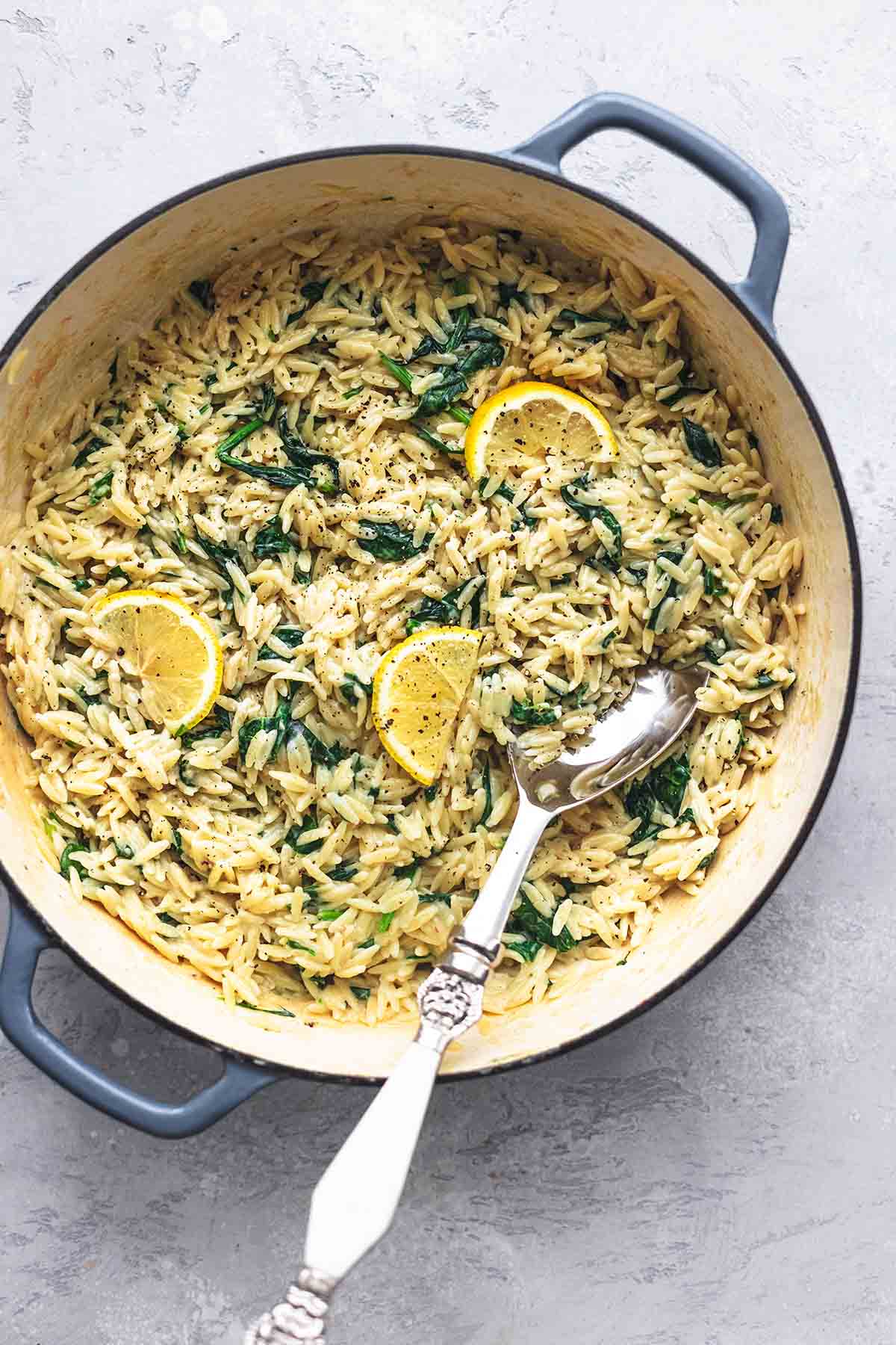 top view of creamy parmesan spinach orzo with a serving spoon in a skillet.