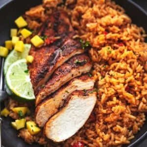 cajun chicken breast sliced with lime wedges and diced mangoes with rice on plate
