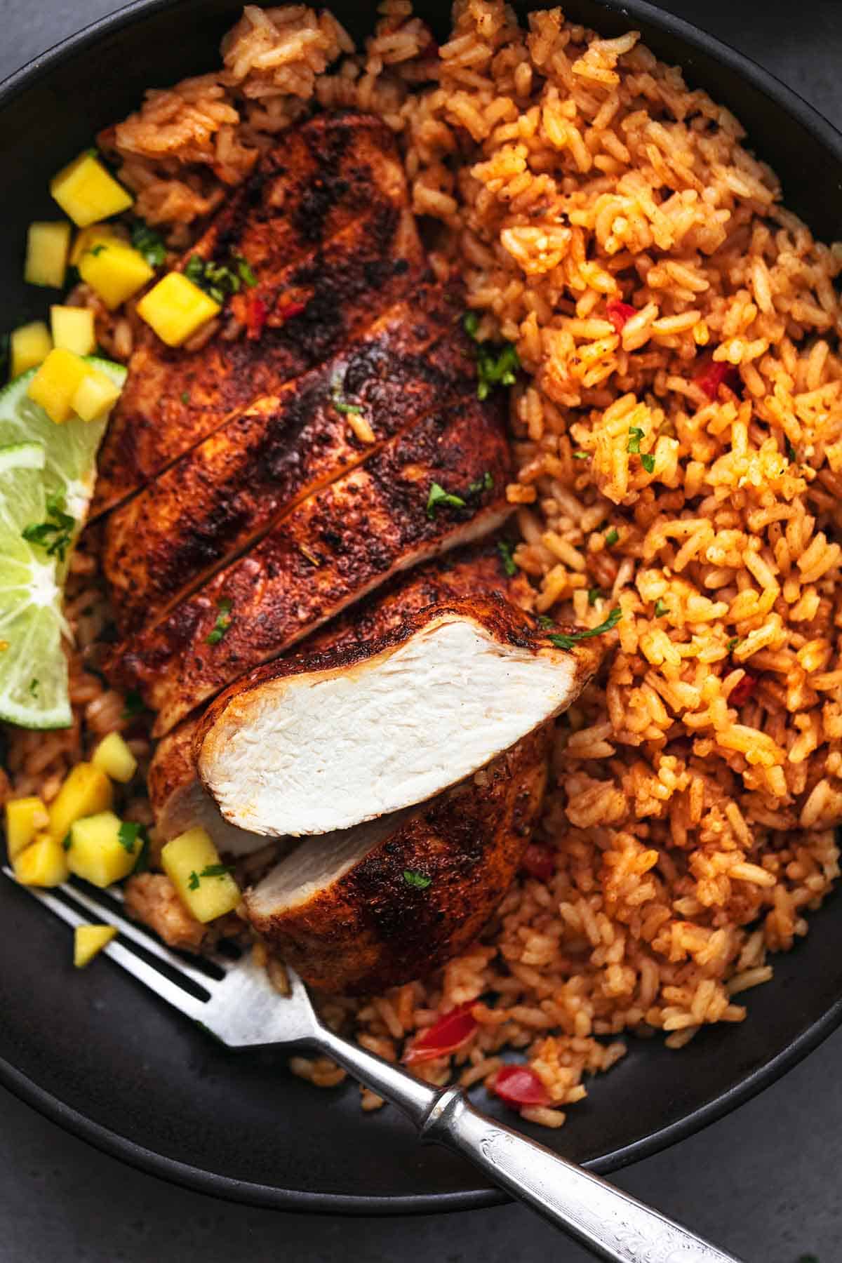 sliced cajun chicken breast with rice and mangoes with fork