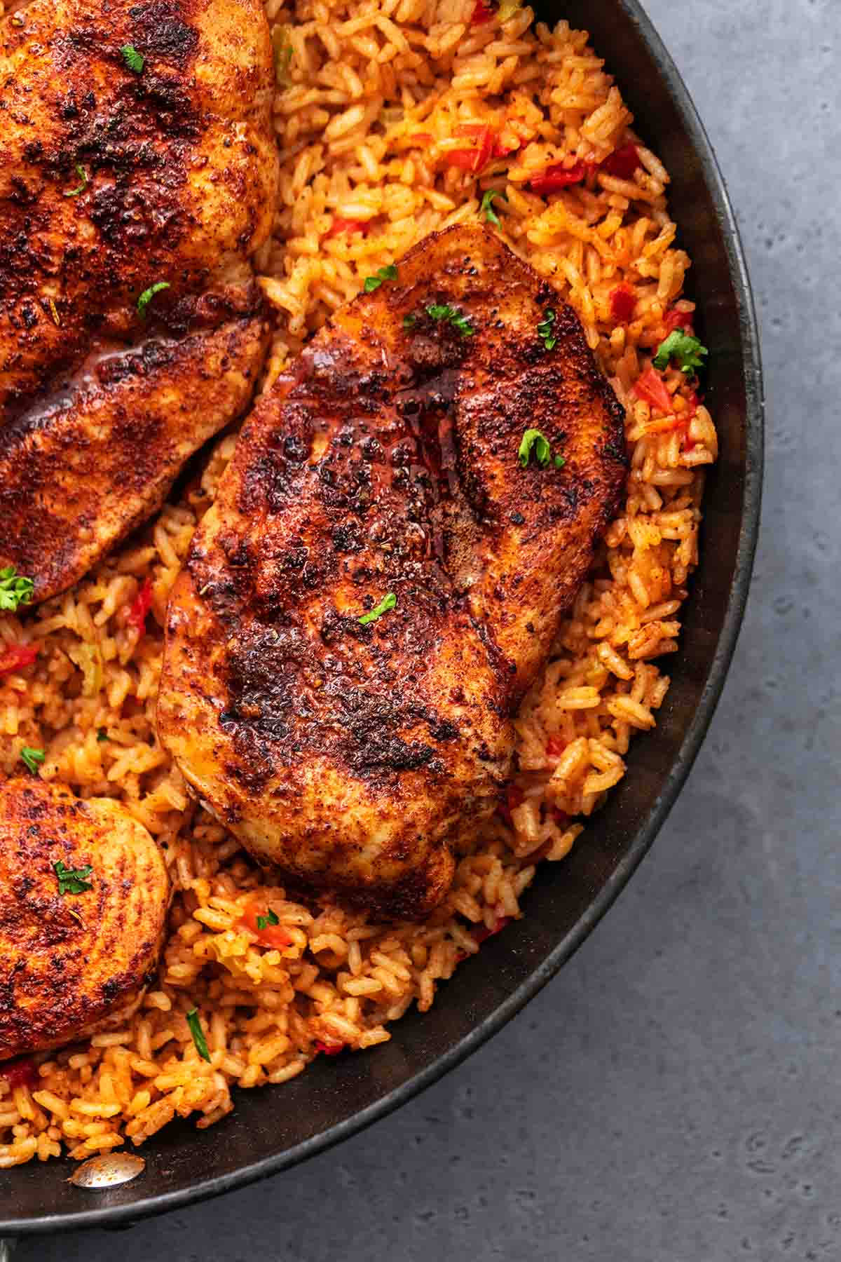 blackened seasoned chicken on top of seasoned rice in skillet