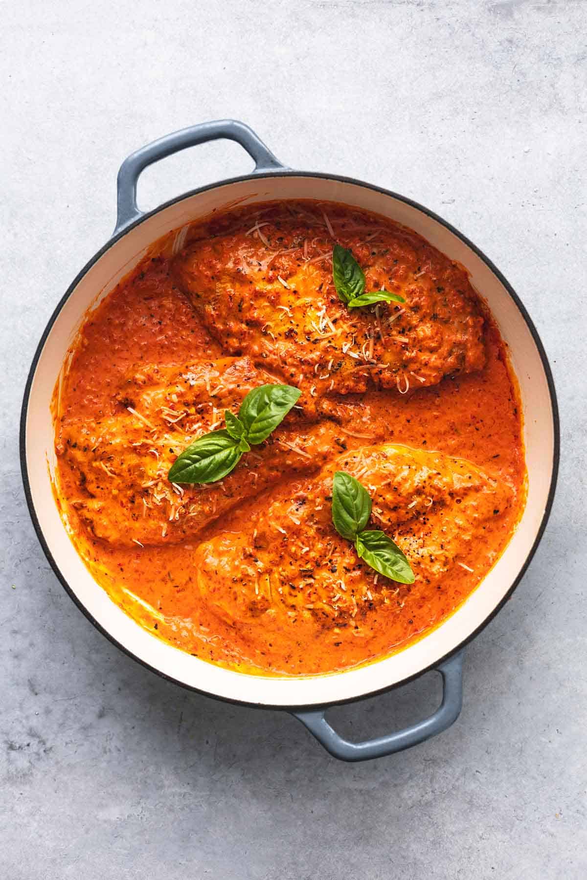 overhead view of three cooked chicken breasts in skillet in sauce with basil leaves