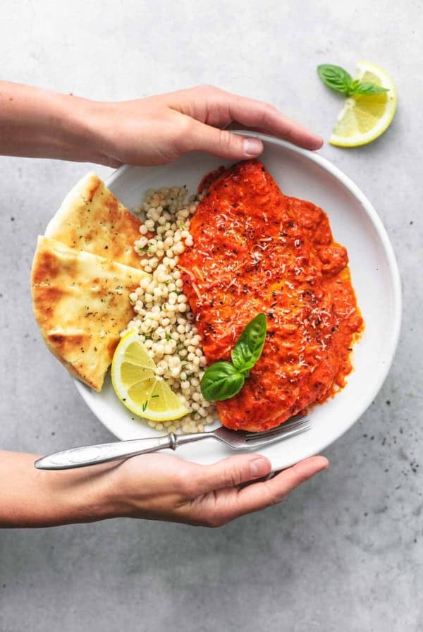 overhead view of hands holding plate of couscous with chicken and pita bread
