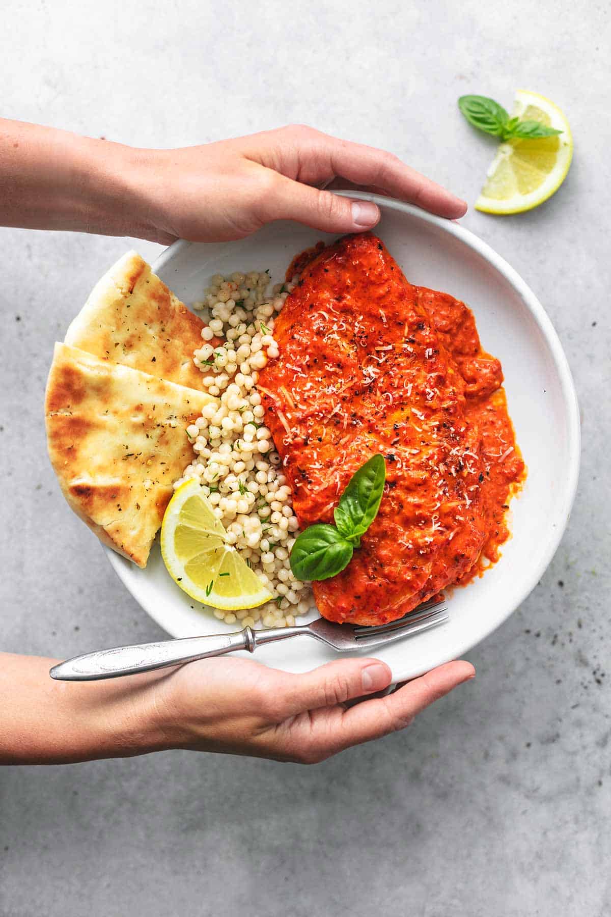 overhead view of hands holding plate of couscous with chicken and pita bread