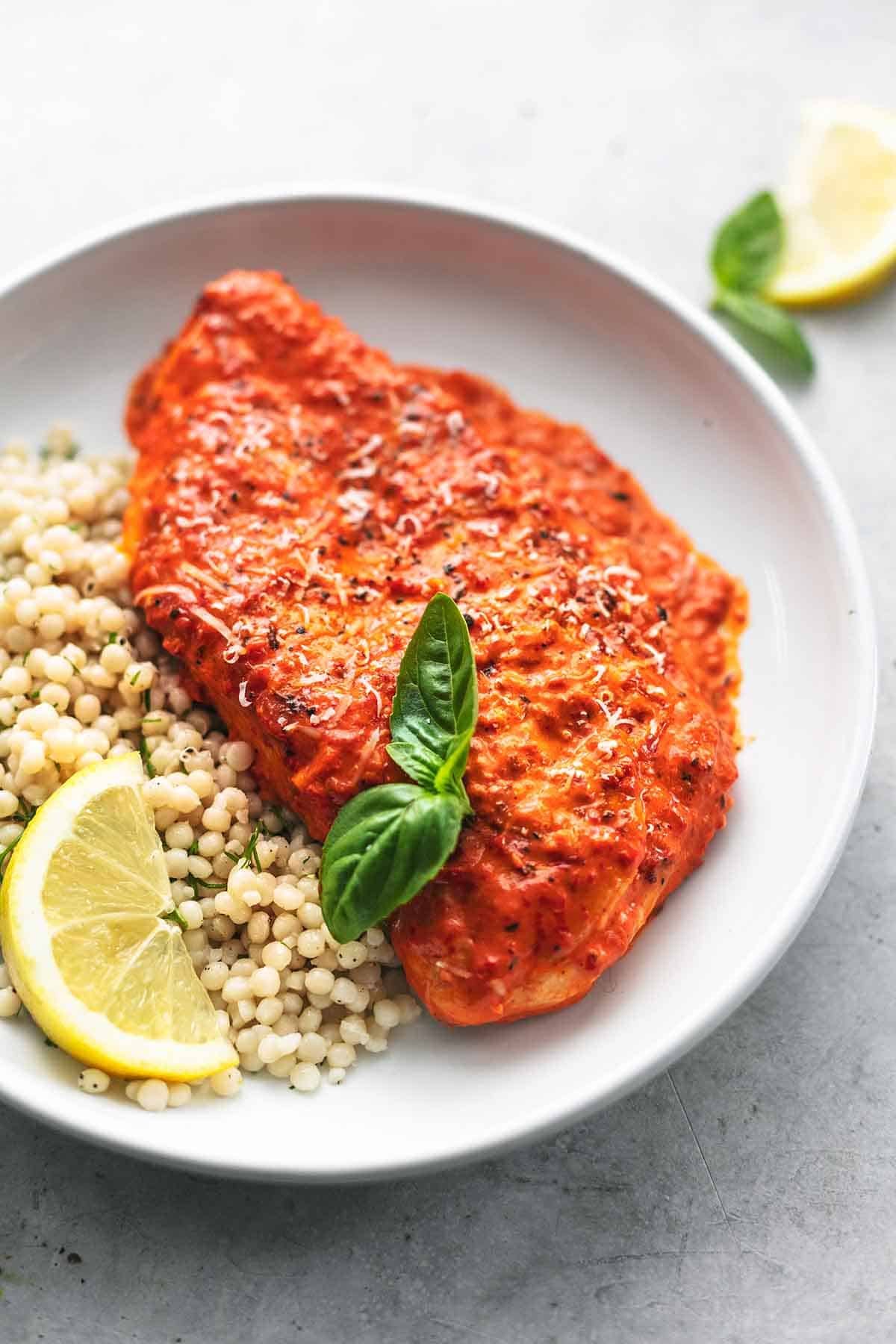 single chicken breast in sauce with fresh basil, lemon wedge, and couscous on plate