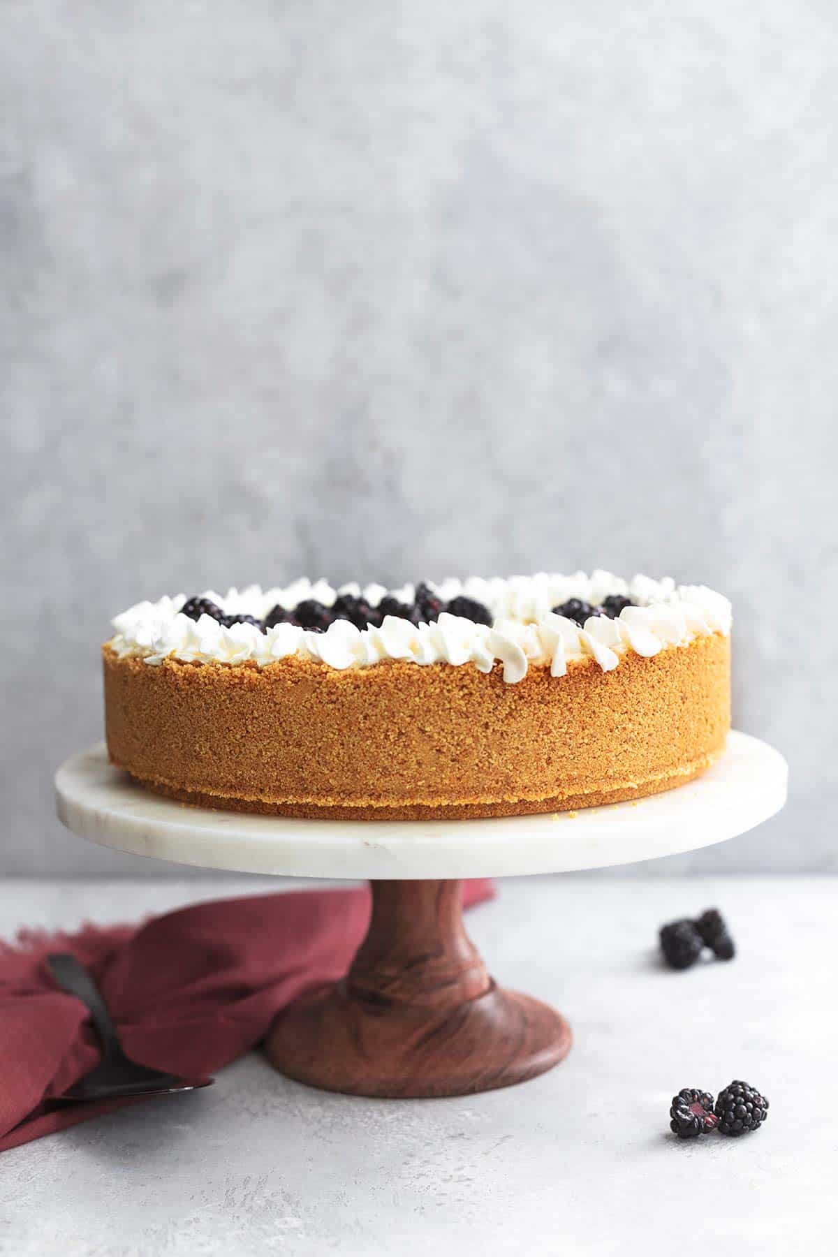 cheesecake on cake stand with black berries on table and red napkin