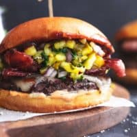 hamburger with bacon, cheese, and pineapple relish on wood cutting board
