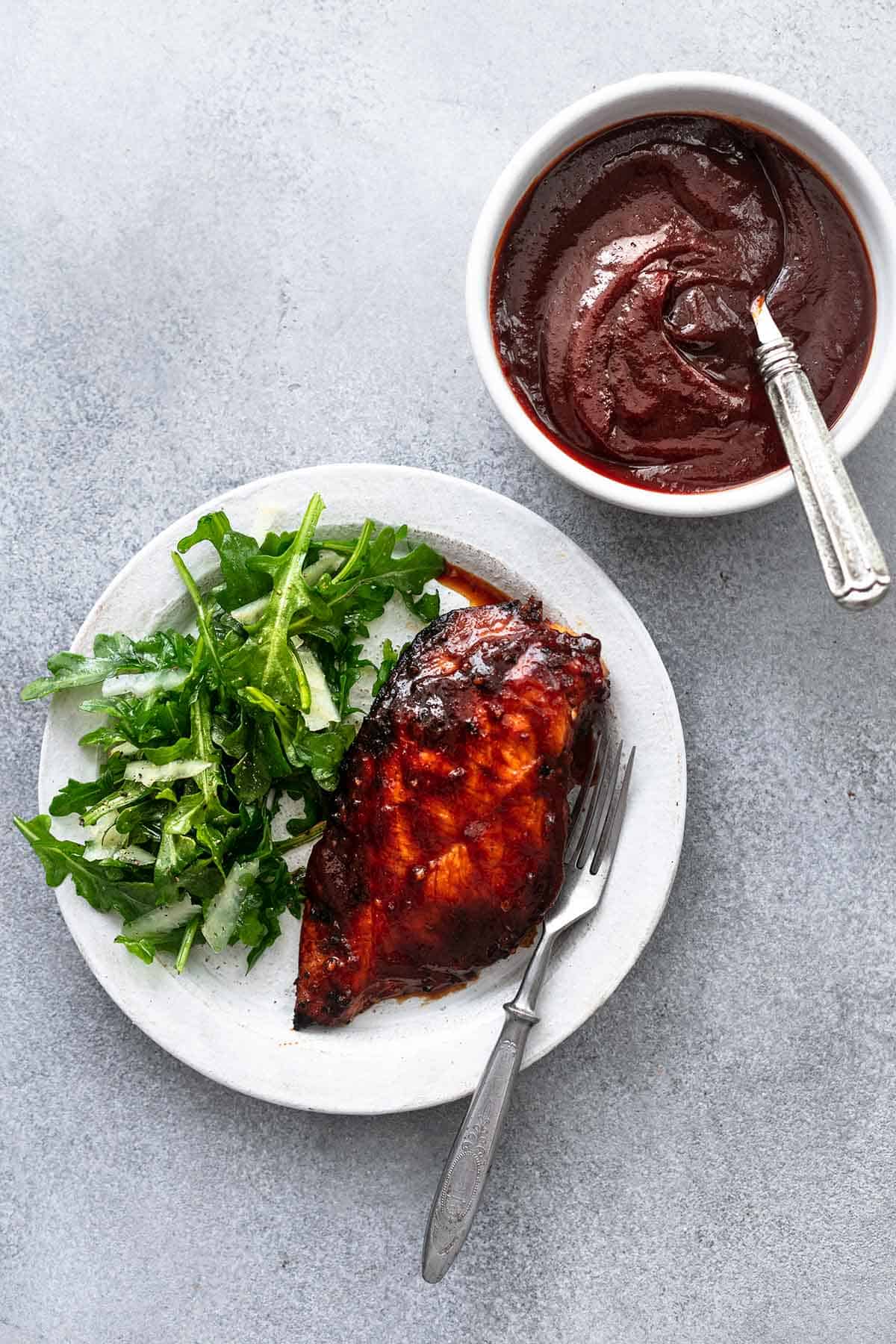 overhead view of plate with chicken and greens and bowl of bbq sauce