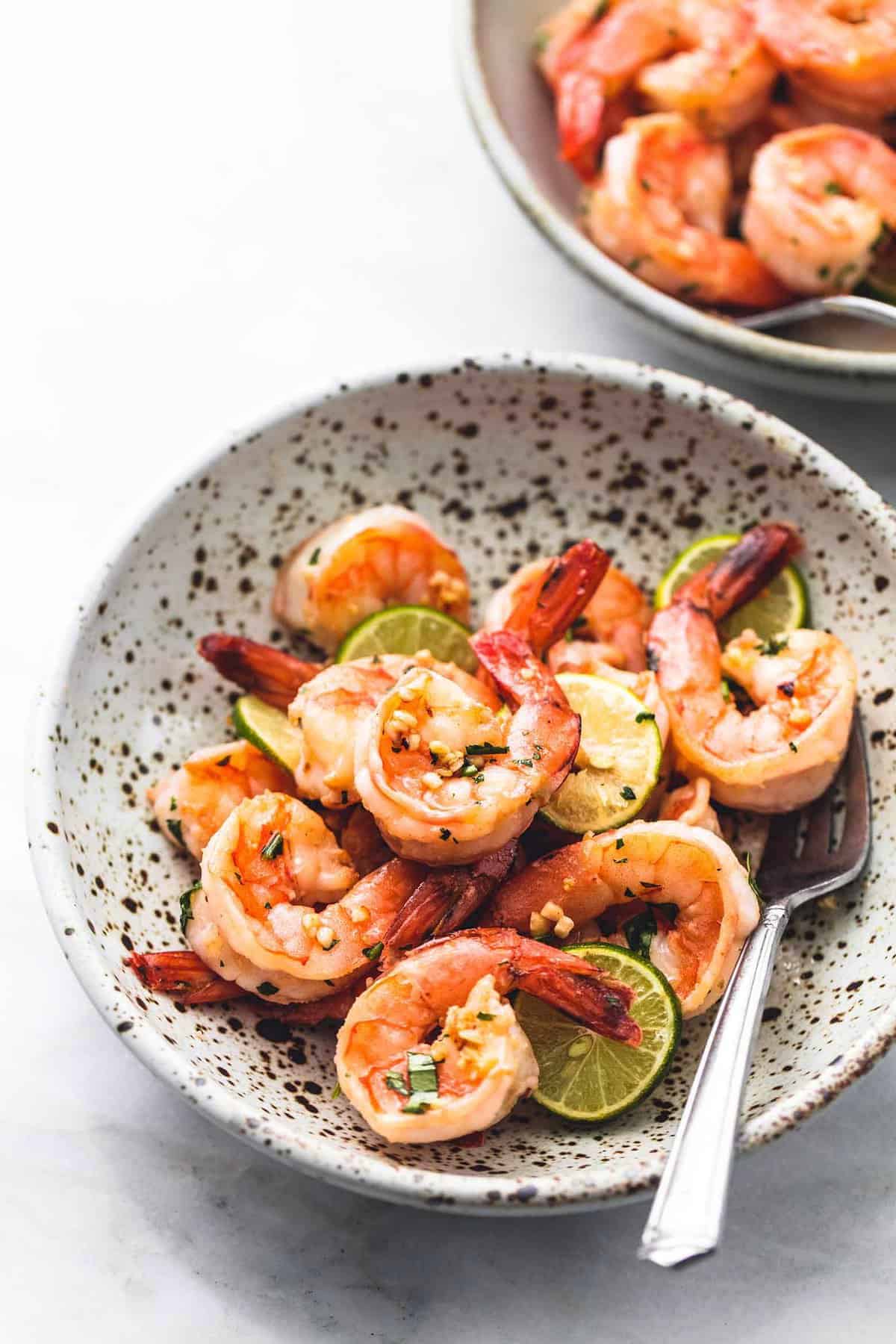 cooked shrimp with lime slices and cilantro in bowl with fork