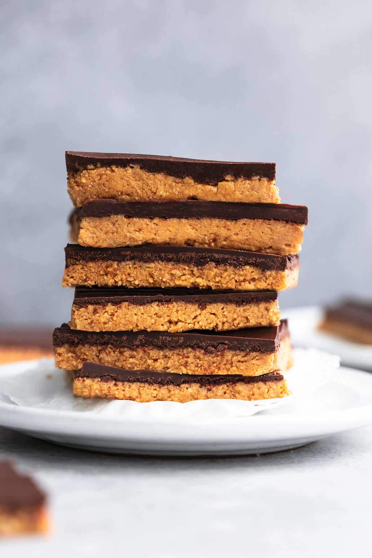 stack of six no bake peanut butter bars on a plate with more bars surrounding on table