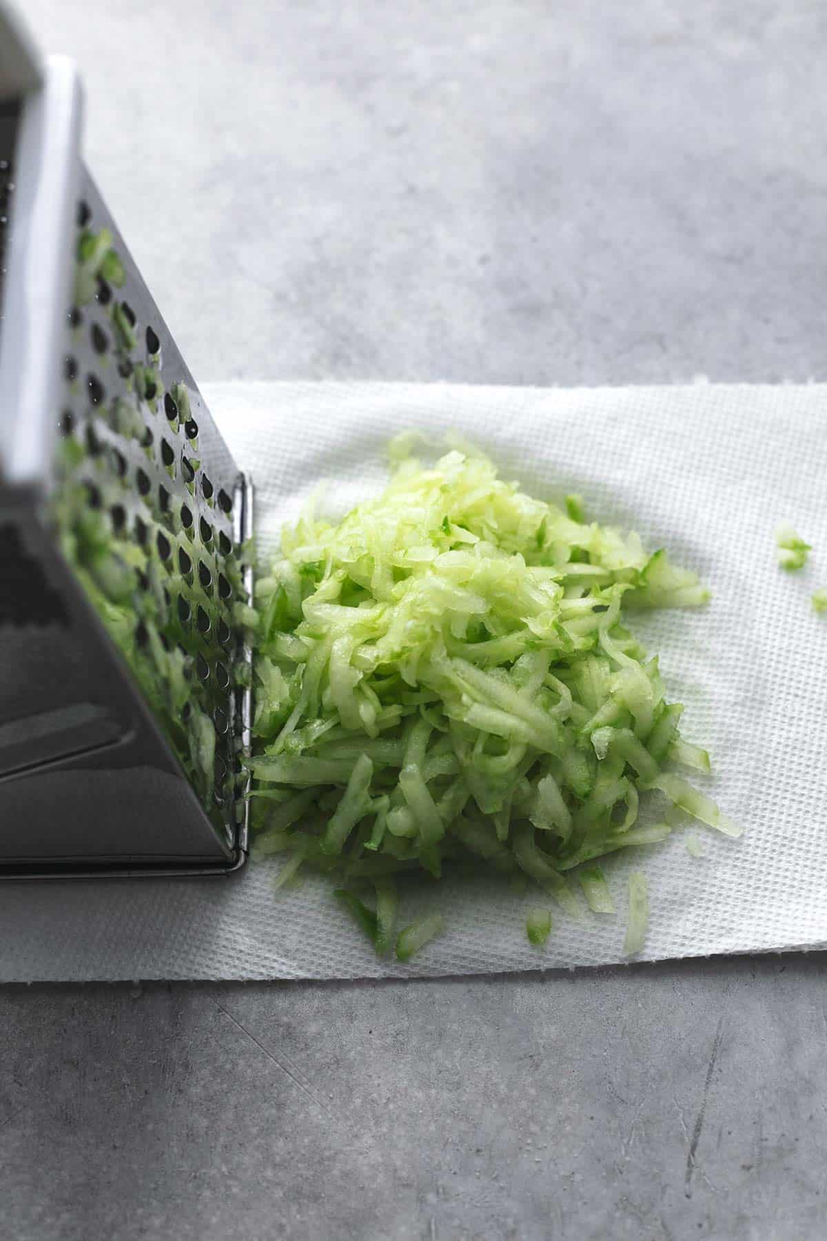 shredded cucumber next to box grater on top of paper towel