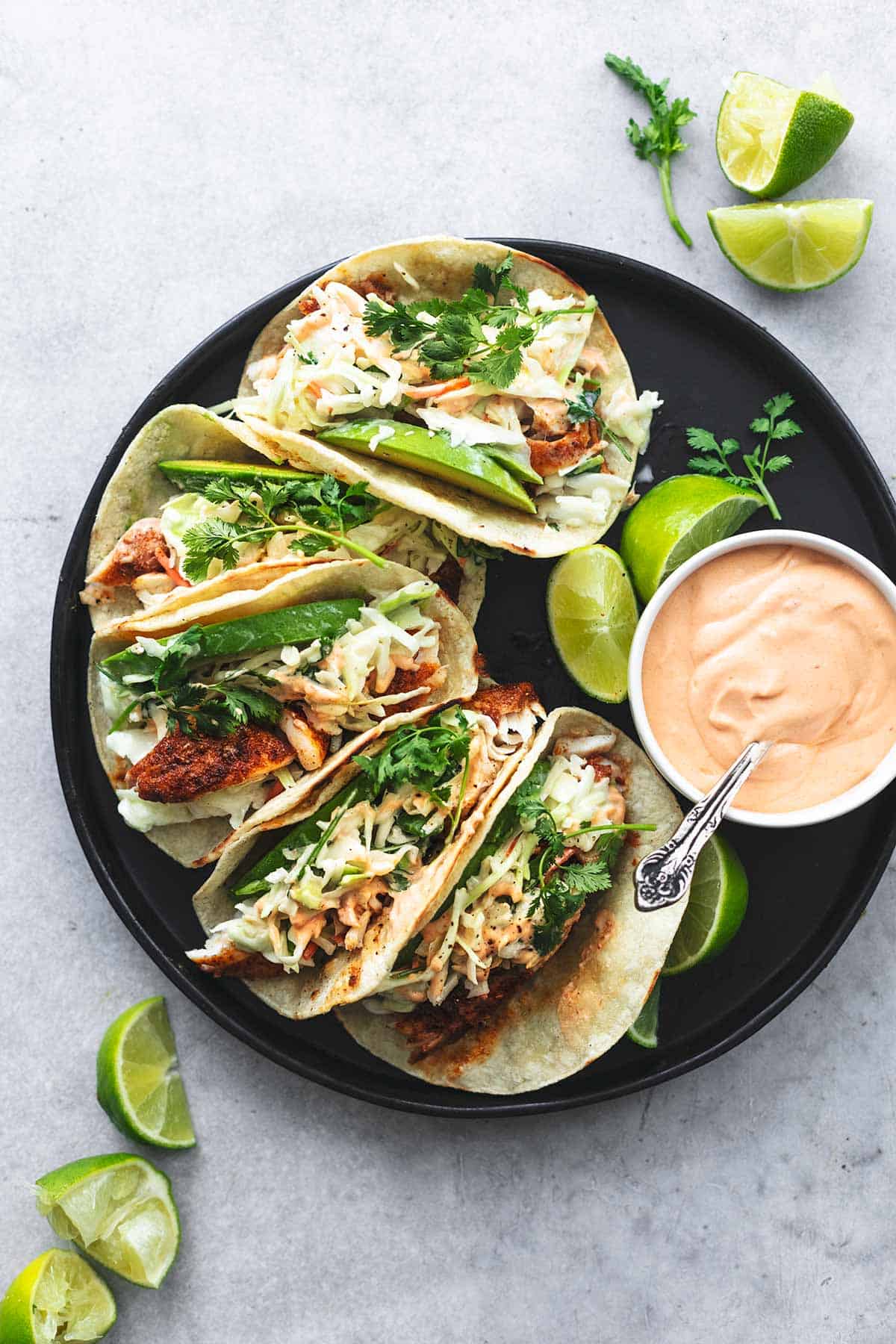 overhead view of five tacos and bowl of sauce with spoon on a plate with lime wedges