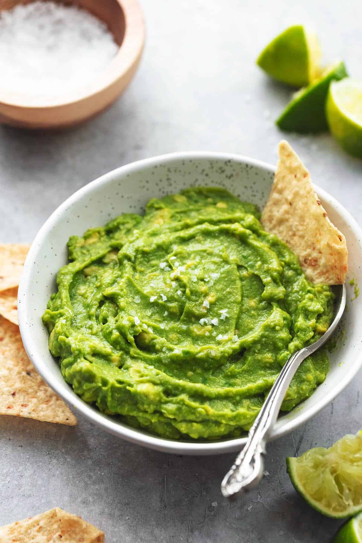 guacamole in a bowl with tortilla chips and lime wedges and