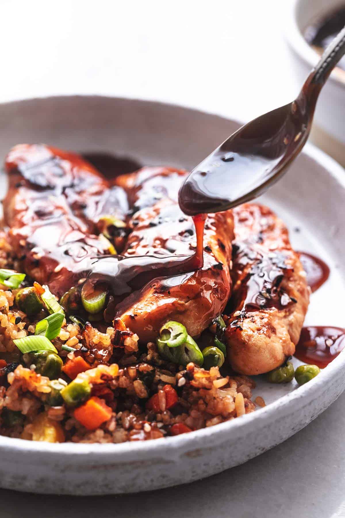 spoon drizzling sauce onto cooked chicken on plate with rice