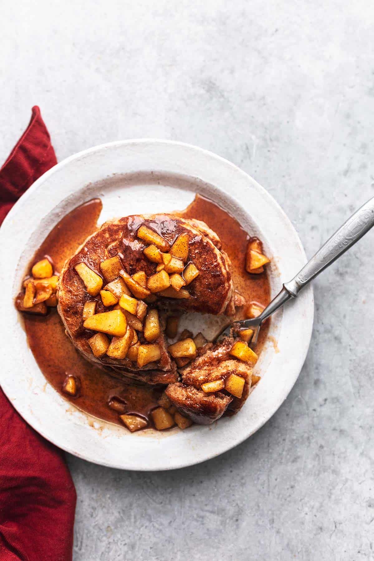 overhead view of fork cutting into stack of pancakes with chopped apples on top