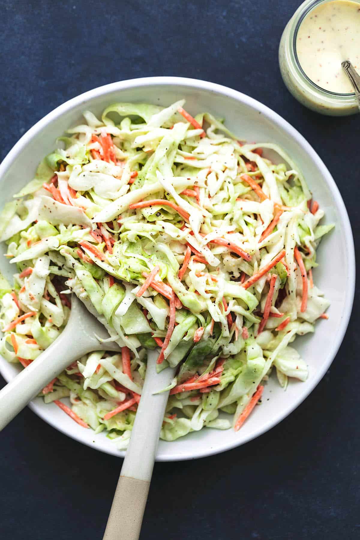 overhead view of coleslaw with serving spoons in platter and jar of sauce