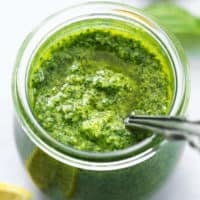 basil pesto sauce with spoon in glass jar with lemons and basil on table