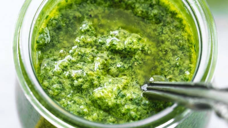 basil pesto sauce with spoon in glass jar with lemons and basil on table