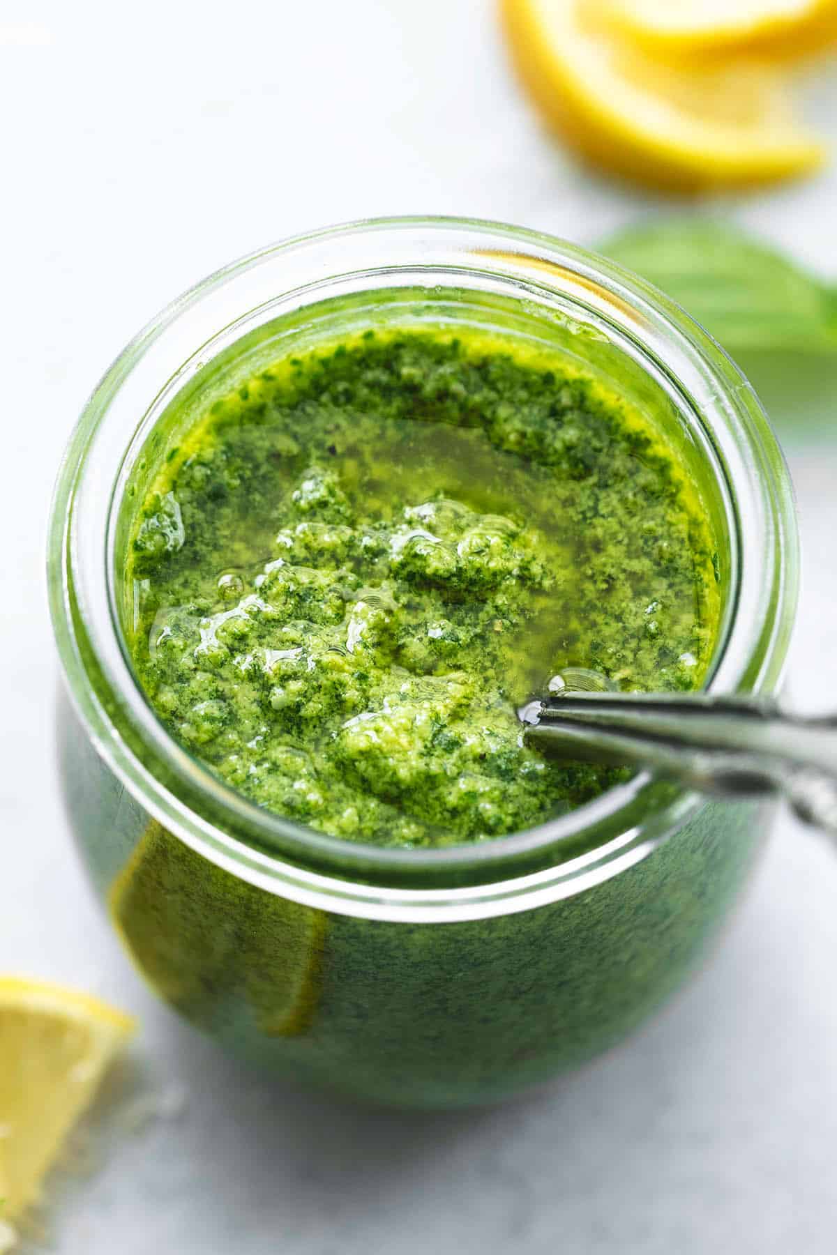 basil pesto sauce with spoon in glass jar with lemons and basil on table