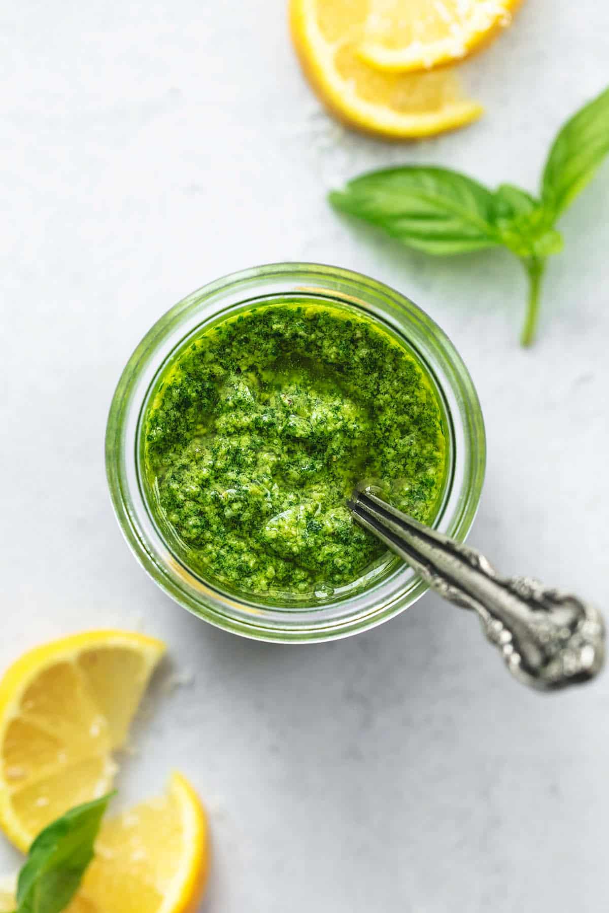 overhead view of jar of pesto with lemon wedges and basil leaves on table