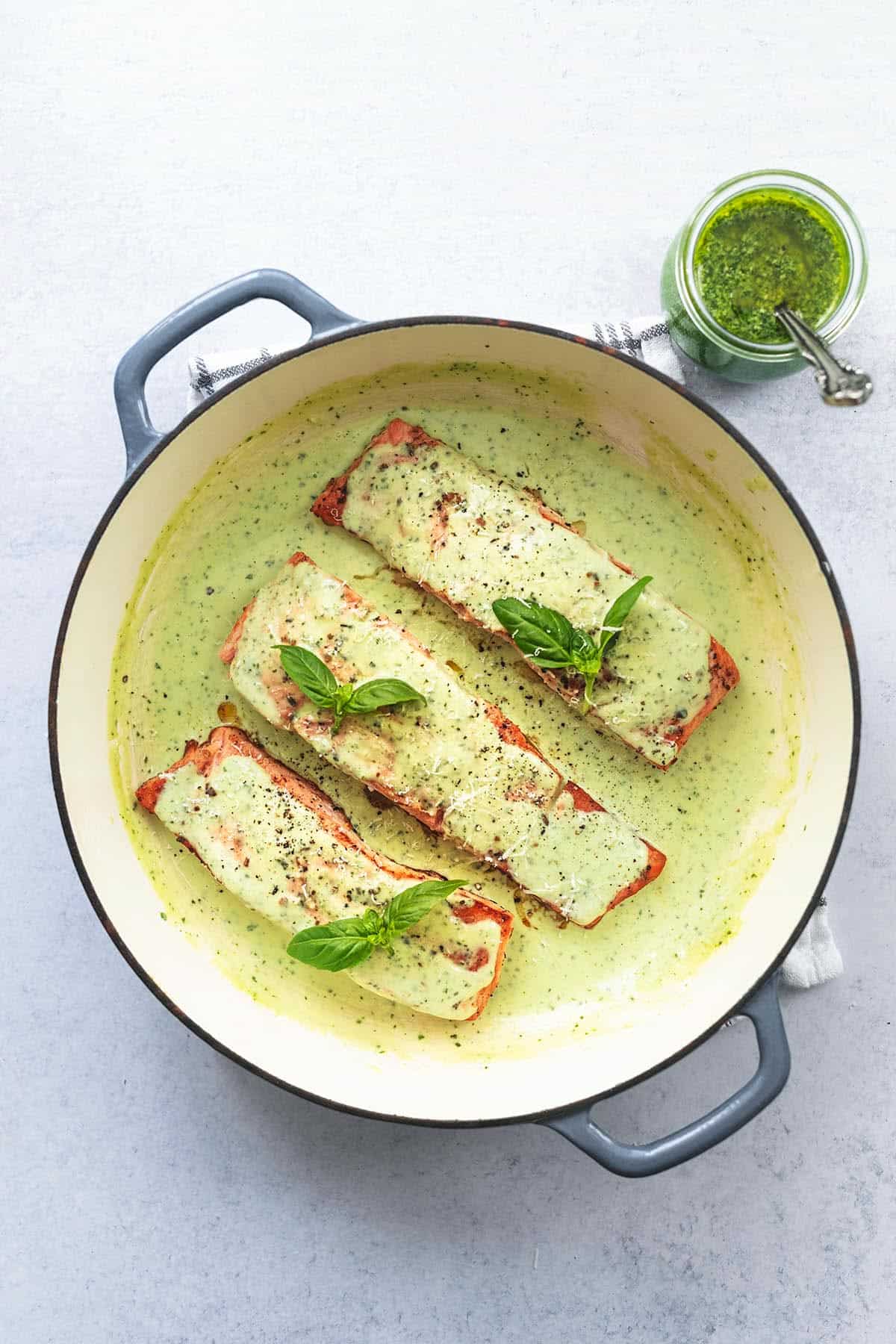 three salmon fillets in skillet with pesto sauce and sauce in jar