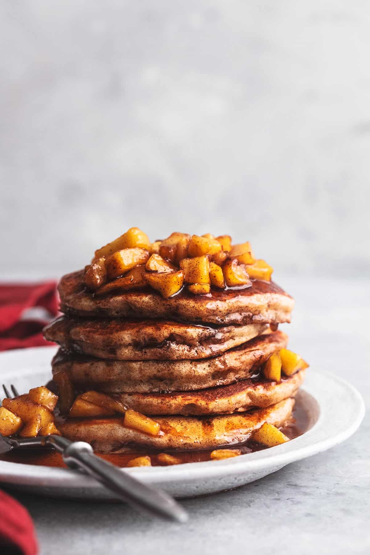 tabletop view of apple cinnamon pancakes stacked on plate with napkin to the side