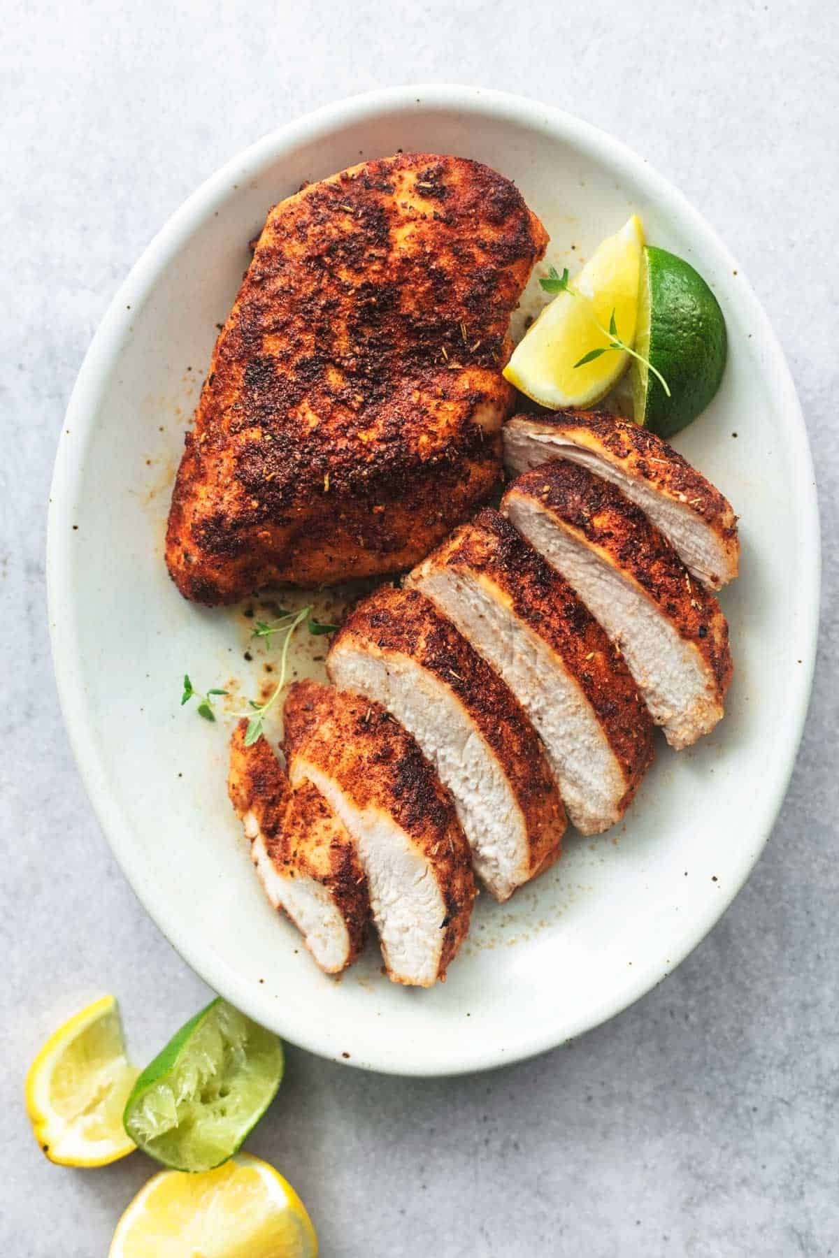 one whole and one sliced chicken breasts with lime wedges on platter