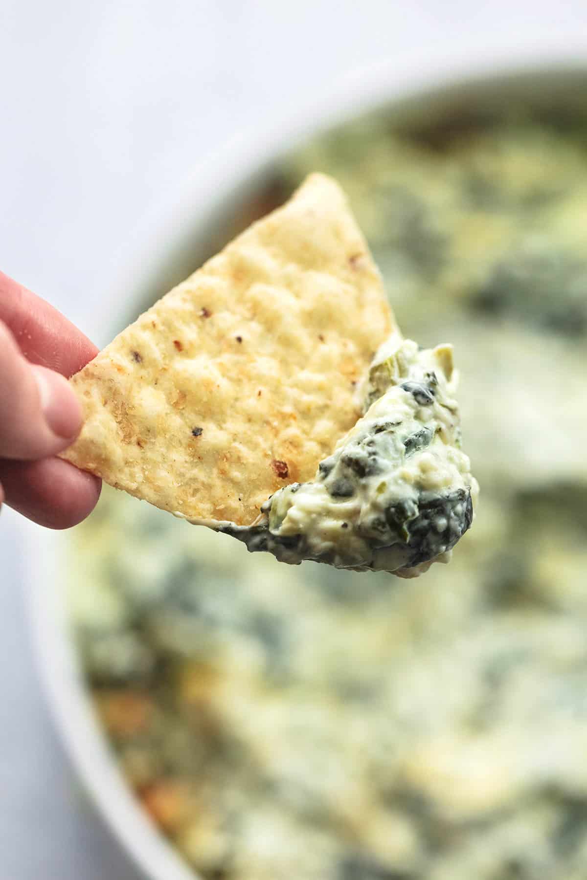 hand scooping tortilla chip into dip