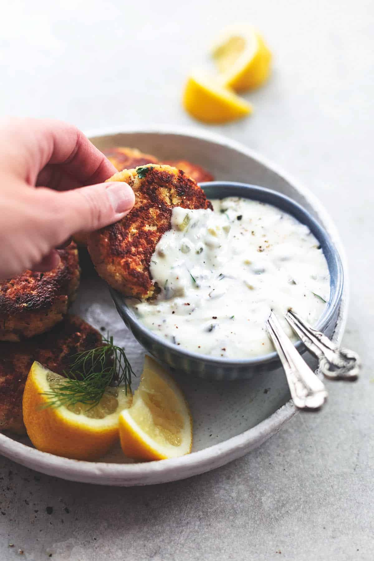 hand dipping crab cake into sauce in bowl