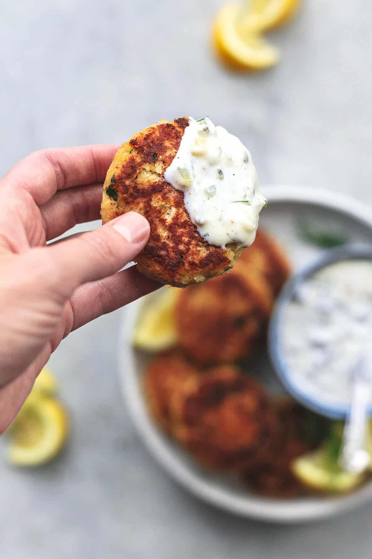 hand holding crab cake dipped in tartar sauce