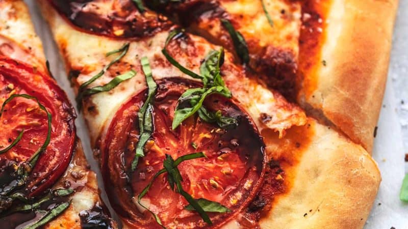 four slices of pizza with tomatoes, cheese, balsamic, and basil
